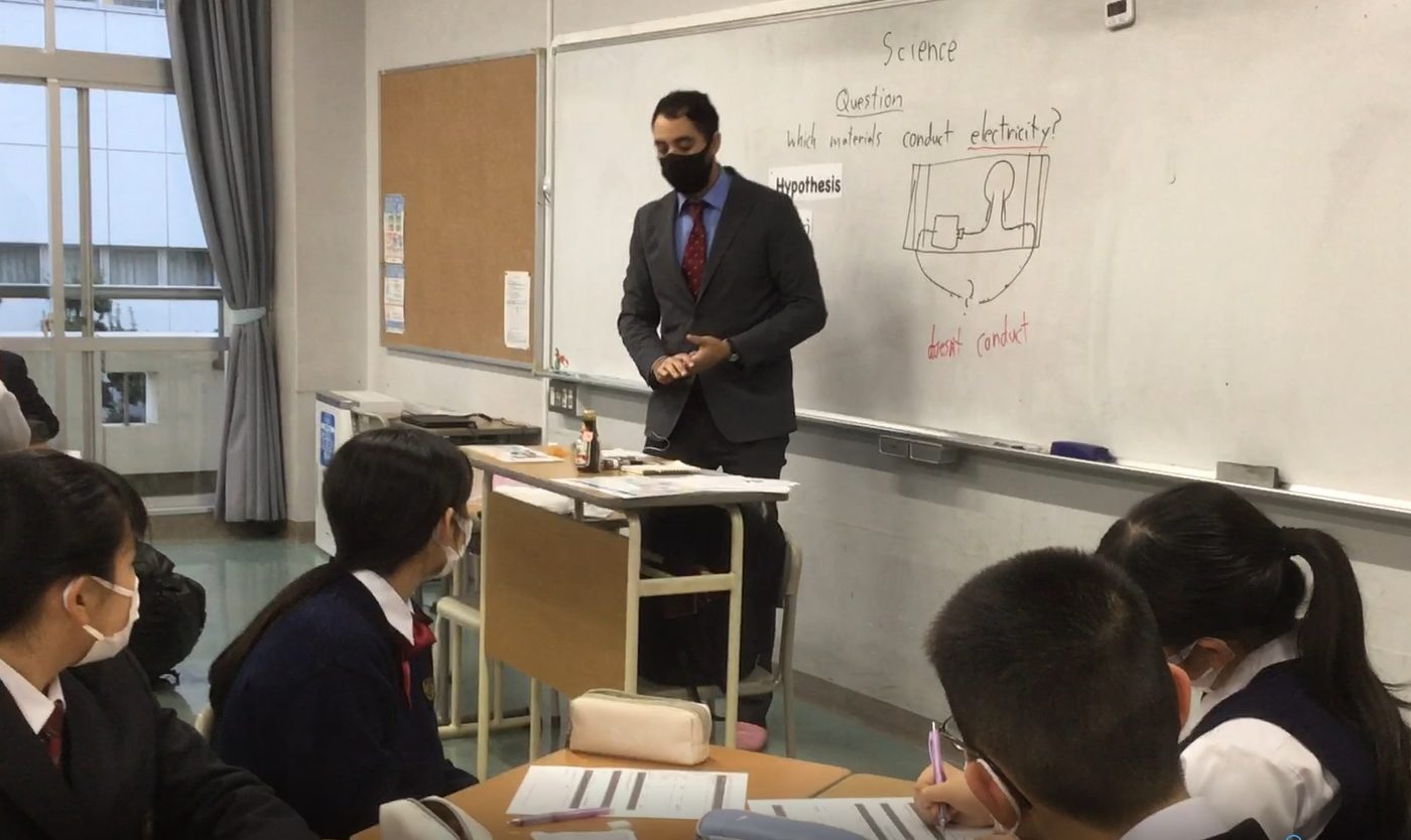 Scienceと書かれたホワイトボードの前で授業をする外国人講師と、制服姿の中学生たち