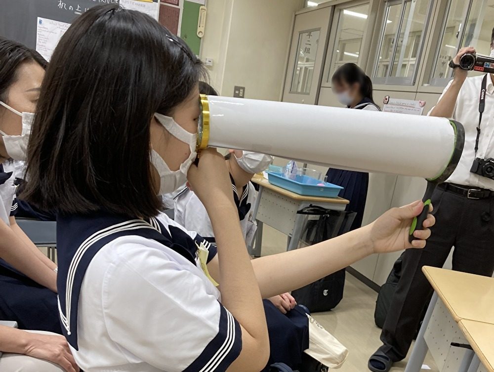 筒状の器具をのぞき込んで観察するセーラー服の中学生