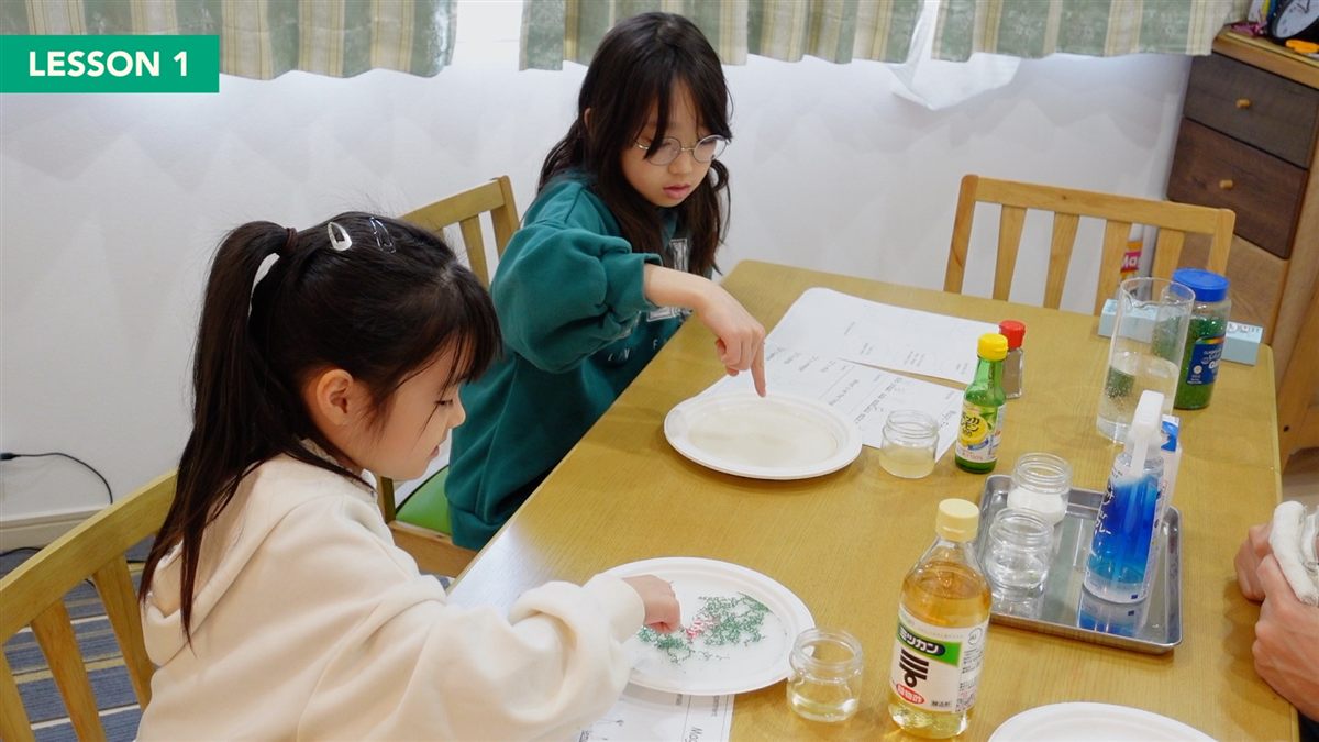 テーブルでコショウと液体を使った実験に取り組むふたりの子ども